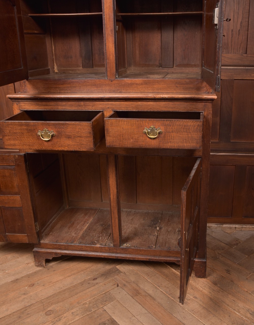 A two-tiered nineteenth-century oak court cupboard featuring panelled doors, drop handles on two upper drawers, and turned finials. View XIV