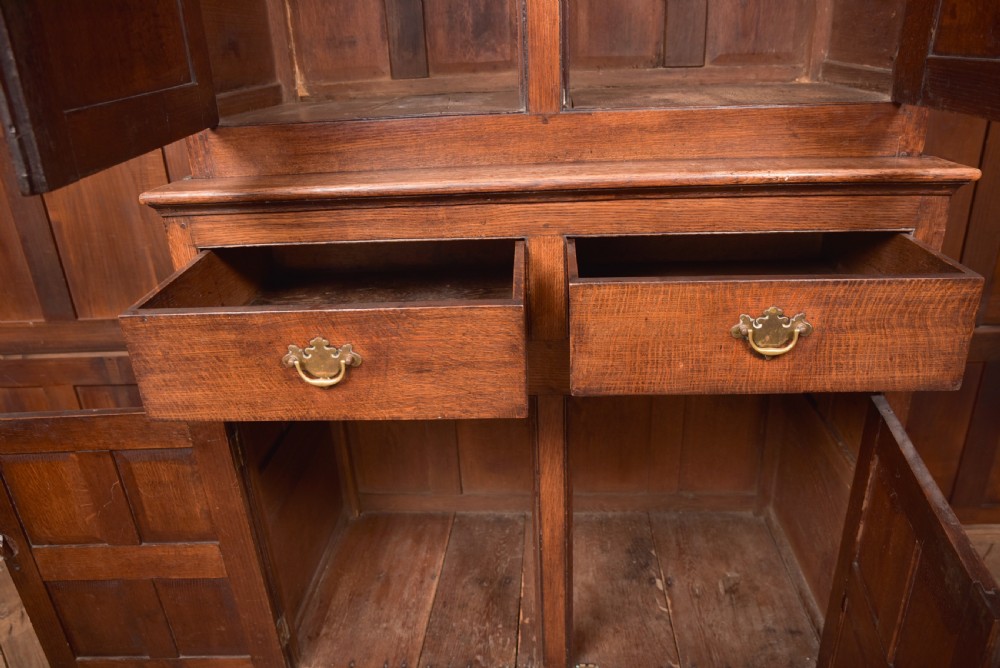 A two-tiered nineteenth-century oak court cupboard featuring panelled doors, drop handles on two upper drawers, and turned finials. View XV