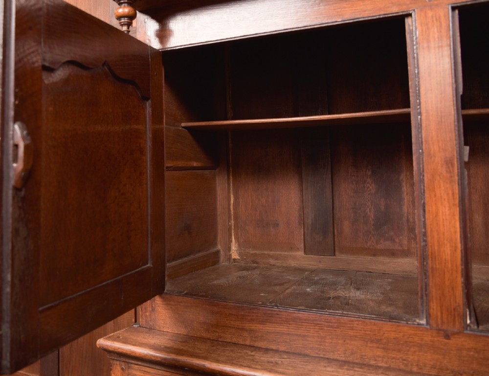 A two-tiered nineteenth-century oak court cupboard featuring panelled doors, drop handles on two upper drawers, and turned finials. View XVI