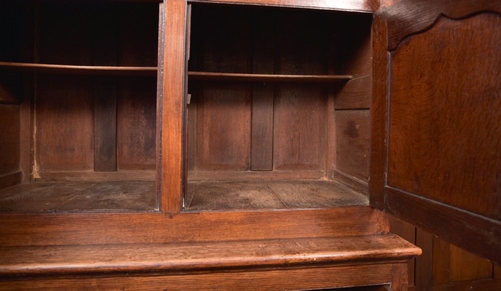 A two-tiered nineteenth-century oak court cupboard featuring panelled doors, drop handles on two upper drawers, and turned finials. View XVII