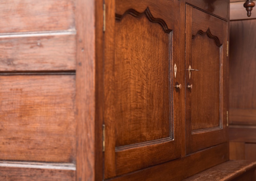 A two-tiered nineteenth-century oak court cupboard featuring panelled doors, drop handles on two upper drawers, and turned finials. View XIX