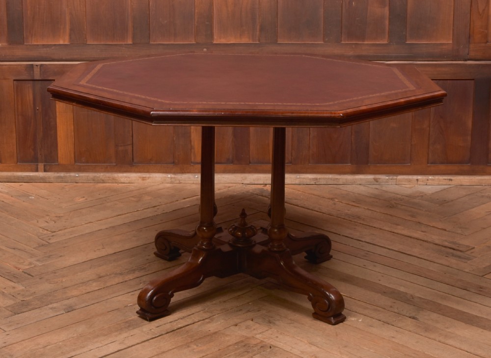 A Victorian octagonal mahogany centre table with a brown leather-inset top, four turned support columns, and a quadruped base with scroll feet.