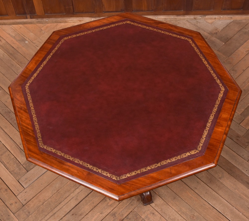 A Victorian octagonal mahogany centre table with a brown leather-inset top, four turned support columns, and a quadruped base with scroll feet. View X