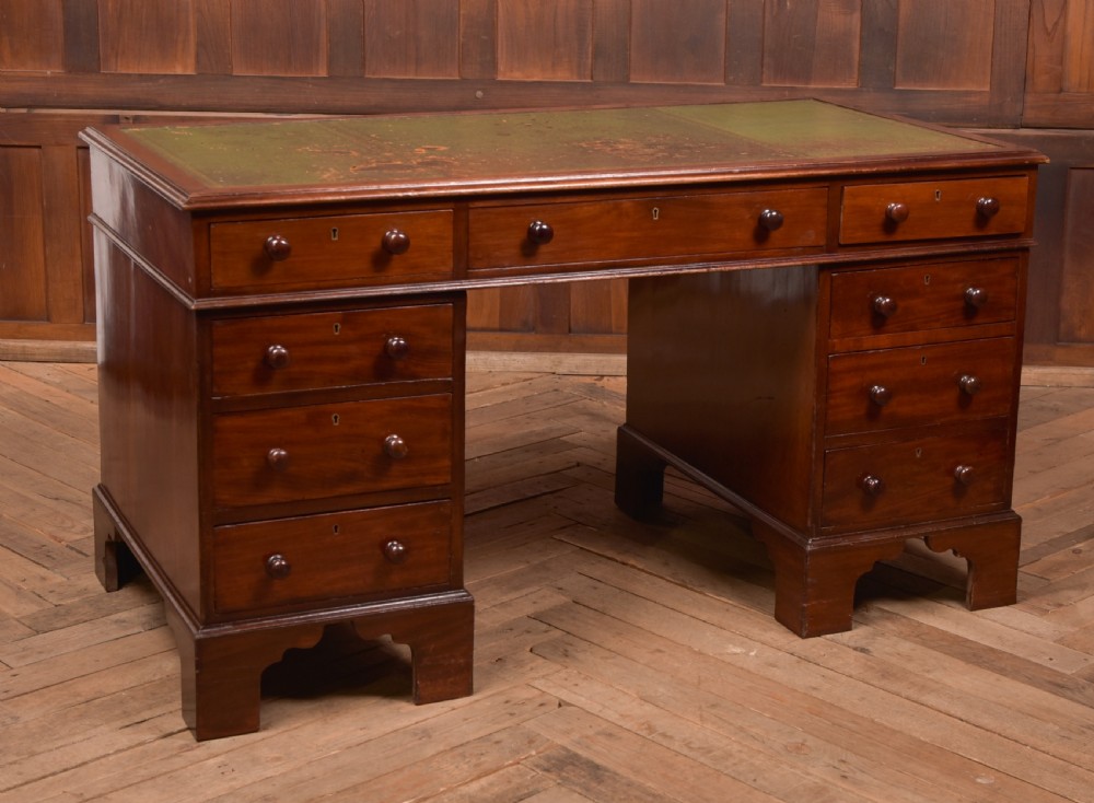 A Victorian mahogany pedestal desk with a green inset leather writing surface, multiple drawers fitted with turned wooden handles, and pedestal bases with bracket feet.