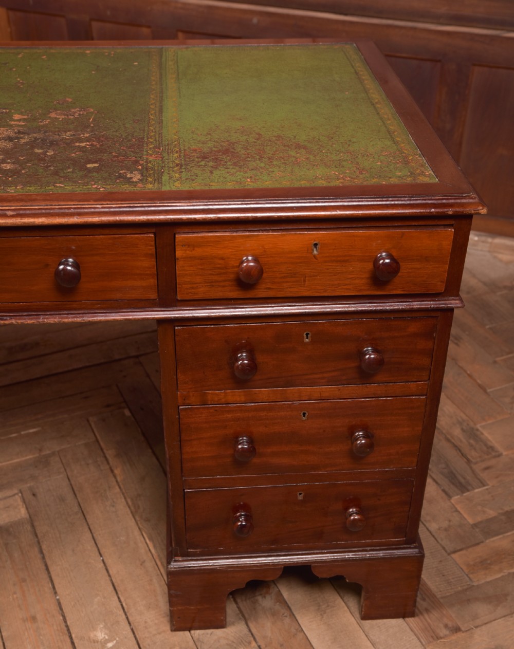A Victorian mahogany pedestal desk with a green inset leather writing surface, multiple drawers fitted with turned wooden handles, and pedestal bases with bracket feet. View VI