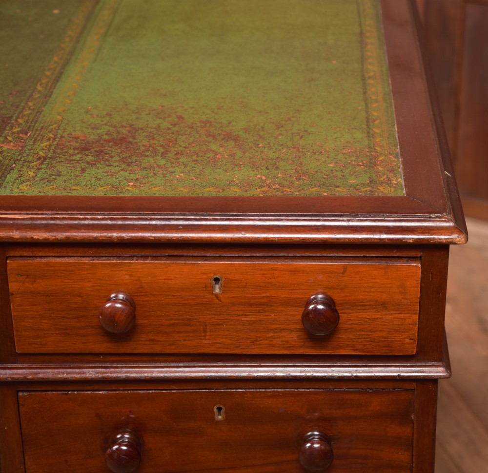 A Victorian mahogany pedestal desk with a green inset leather writing surface, multiple drawers fitted with turned wooden handles, and pedestal bases with bracket feet. View VII