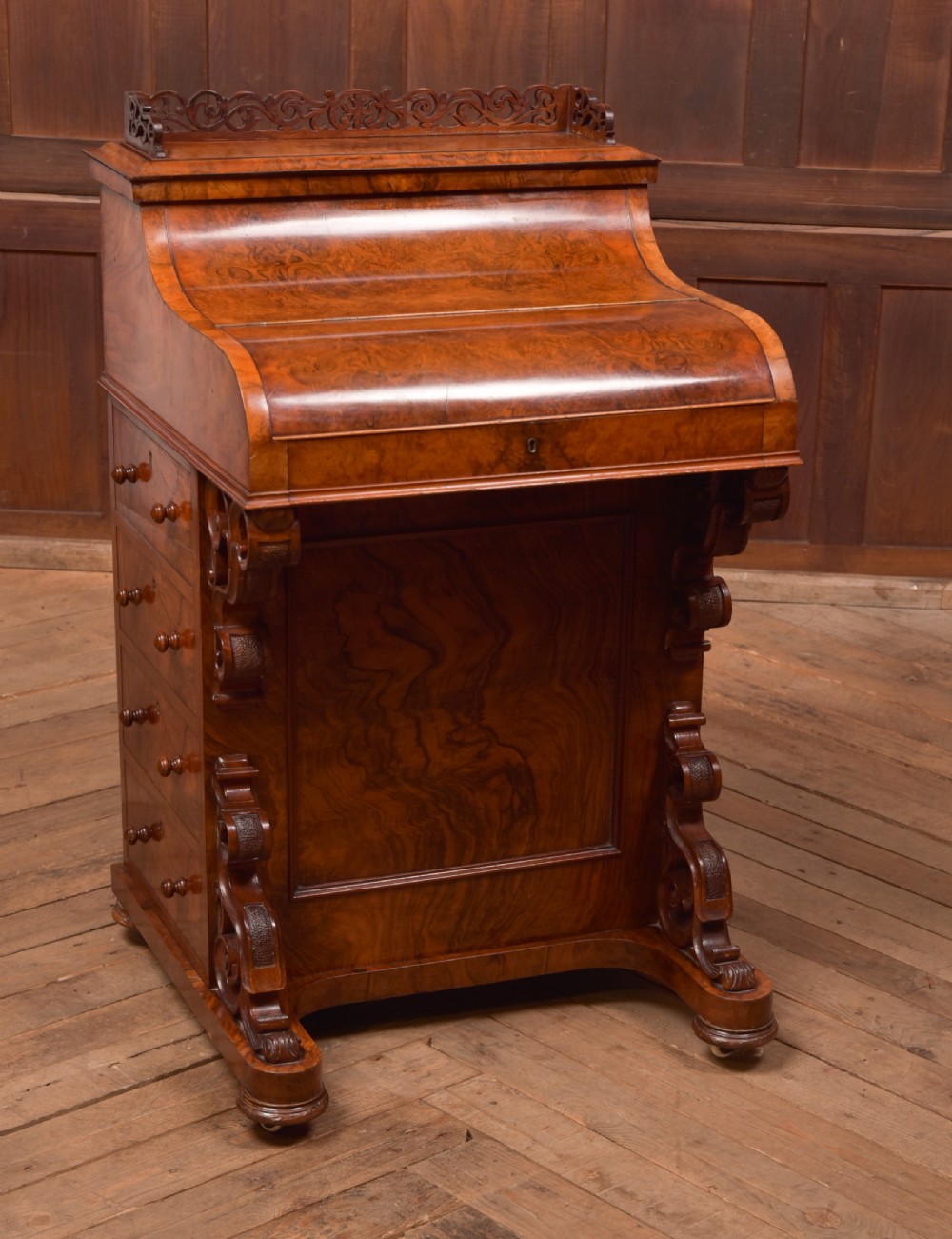 A Victorian burr walnut piano top Davenport desk featuring a carved fretwork gallery, sloped writing lid, scroll front supports, and side-opening drawers.