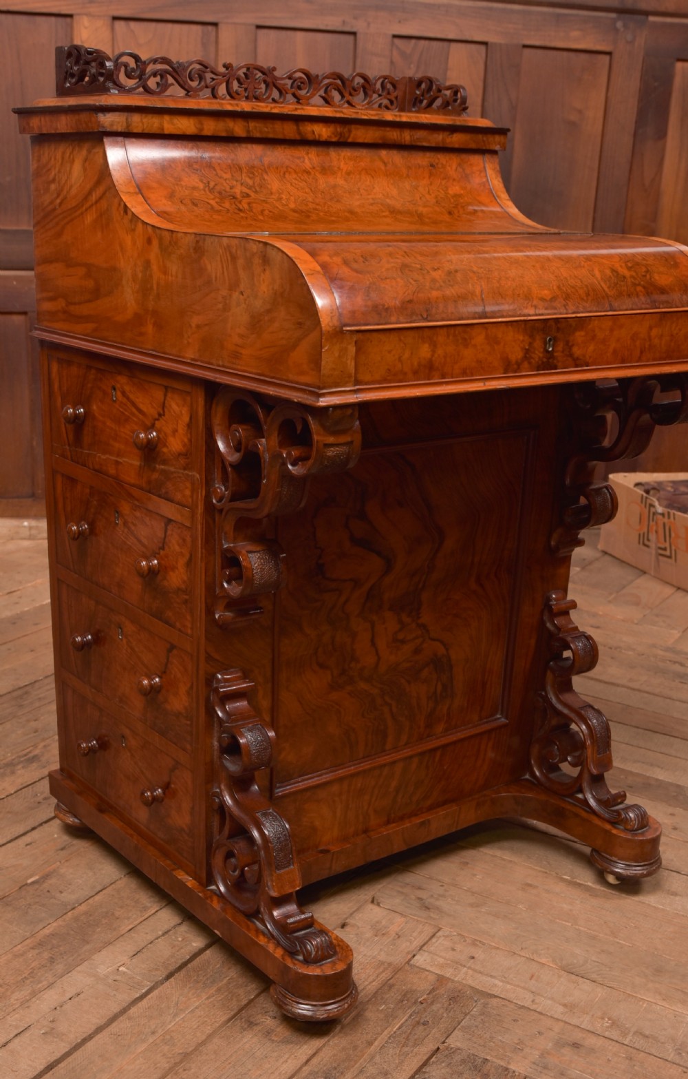 A Victorian burr walnut piano top Davenport desk featuring a carved fretwork gallery, sloped writing lid, scroll front supports, and side-opening drawers. View II