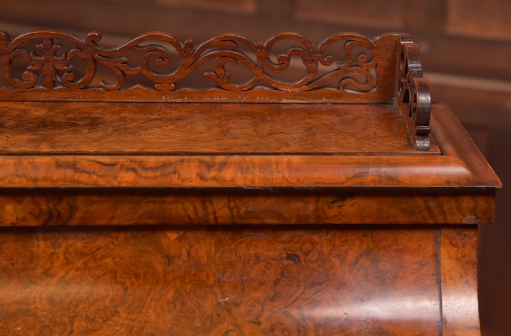 A Victorian burr walnut piano top Davenport desk featuring a carved fretwork gallery, sloped writing lid, scroll front supports, and side-opening drawers. View III