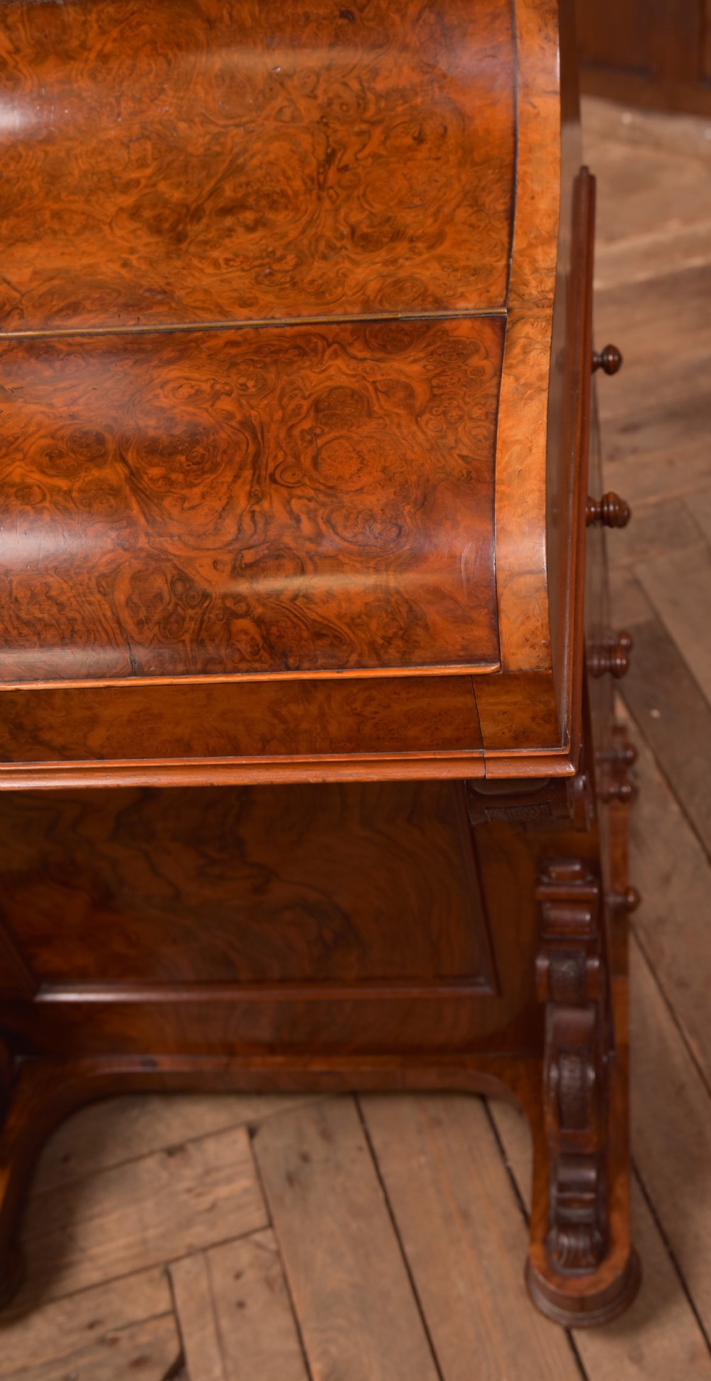 A Victorian burr walnut piano top Davenport desk featuring a carved fretwork gallery, sloped writing lid, scroll front supports, and side-opening drawers. View V