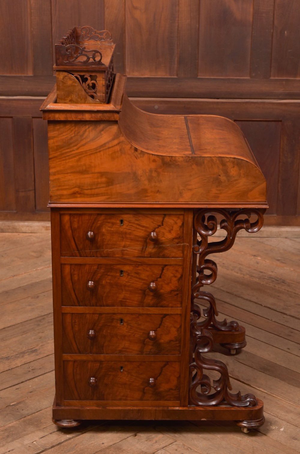 A Victorian burr walnut piano top Davenport desk featuring a carved fretwork gallery, sloped writing lid, scroll front supports, and side-opening drawers. View VII