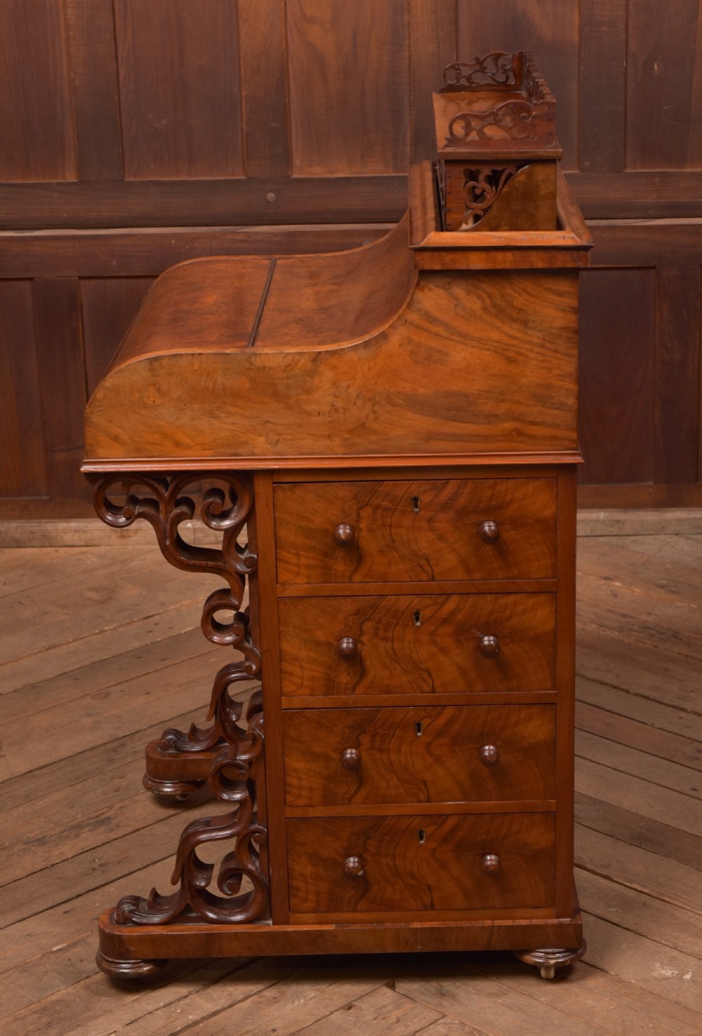 A Victorian burr walnut piano top Davenport desk featuring a carved fretwork gallery, sloped writing lid, scroll front supports, and side-opening drawers. View IX