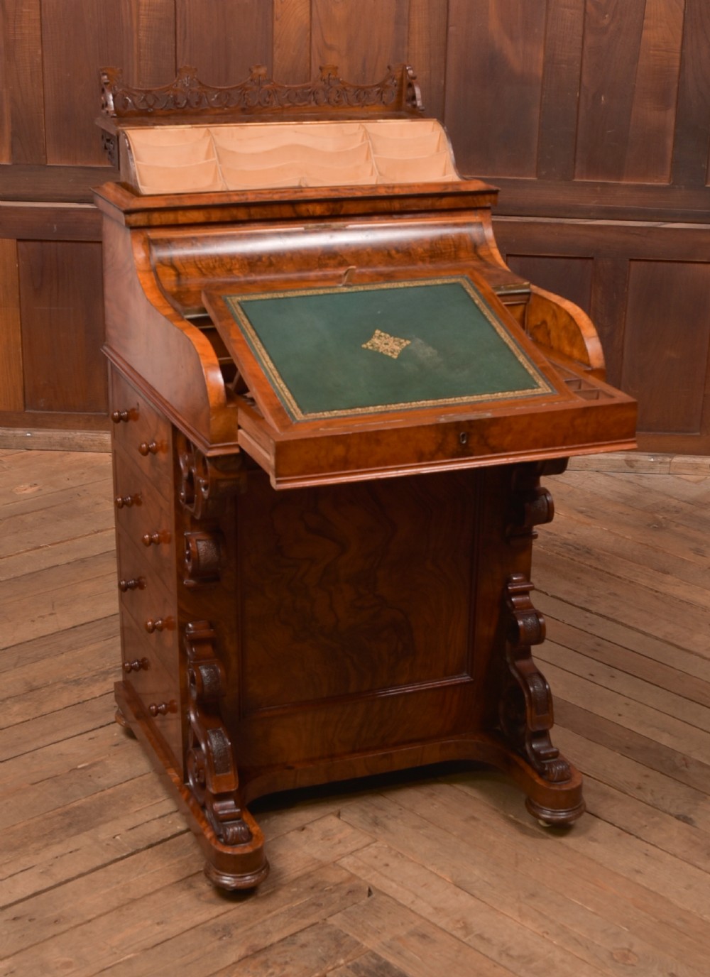 A Victorian burr walnut piano top Davenport desk featuring a carved fretwork gallery, sloped writing lid, scroll front supports, and side-opening drawers. View X