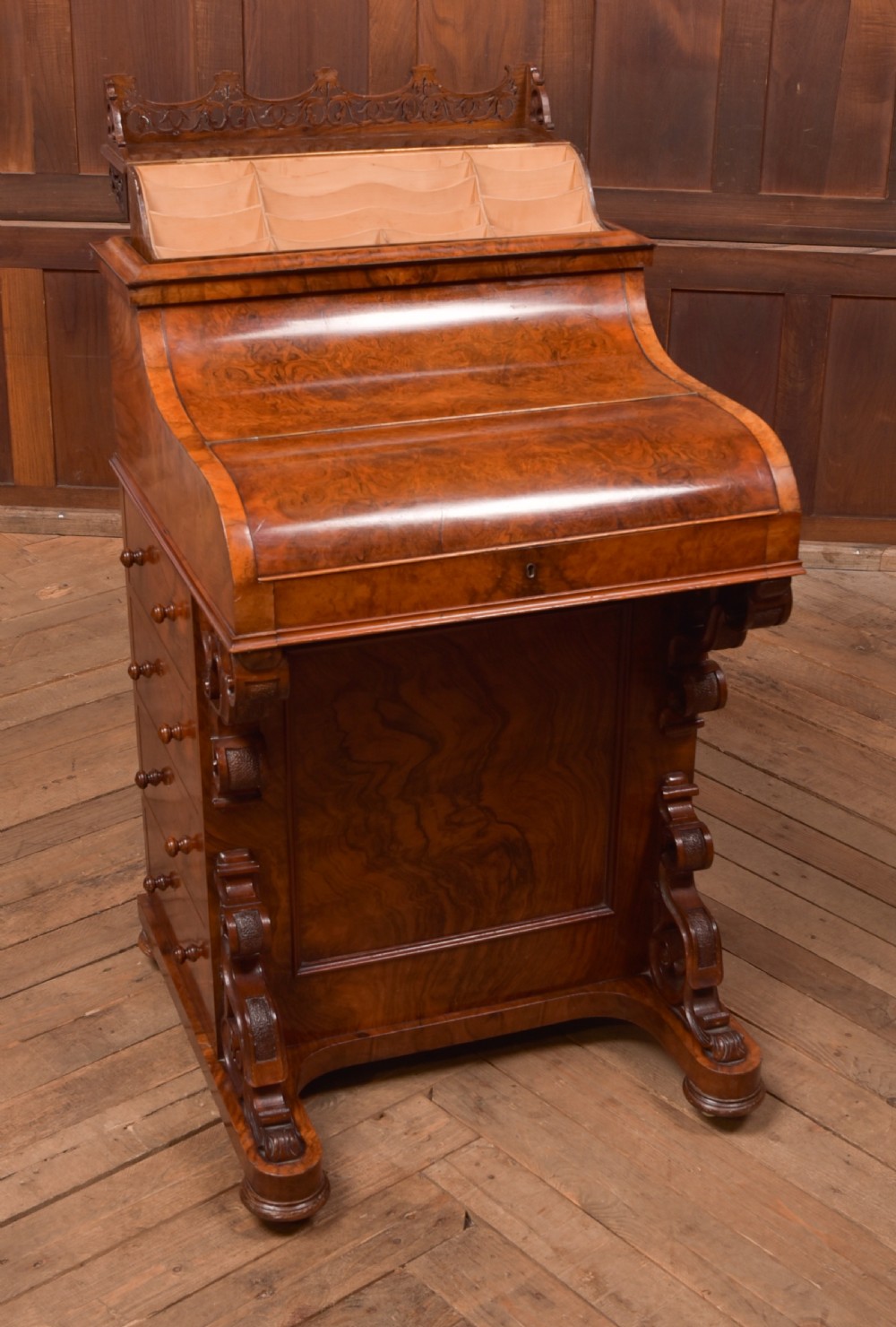 A Victorian burr walnut piano top Davenport desk featuring a carved fretwork gallery, sloped writing lid, scroll front supports, and side-opening drawers. View XII