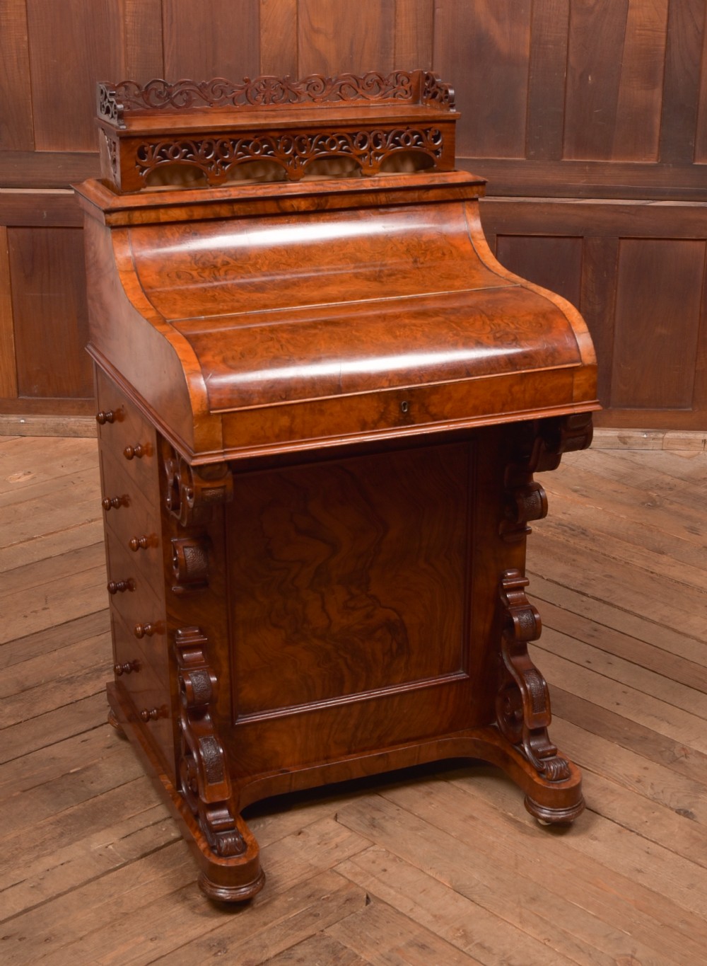 A Victorian burr walnut piano top Davenport desk featuring a carved fretwork gallery, sloped writing lid, scroll front supports, and side-opening drawers. View XIII