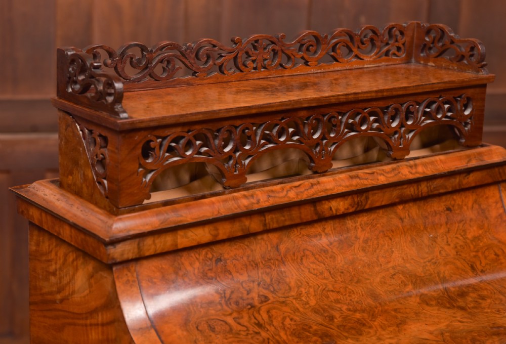 A Victorian burr walnut piano top Davenport desk featuring a carved fretwork gallery, sloped writing lid, scroll front supports, and side-opening drawers. View XVII