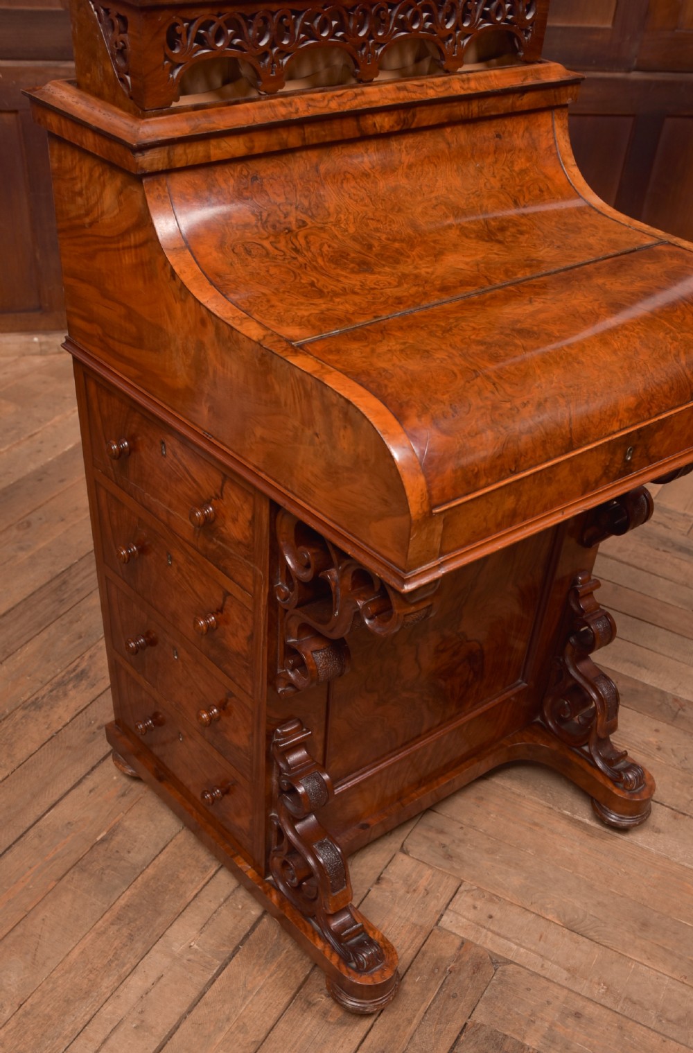 A Victorian burr walnut piano top Davenport desk featuring a carved fretwork gallery, sloped writing lid, scroll front supports, and side-opening drawers. View XVIII