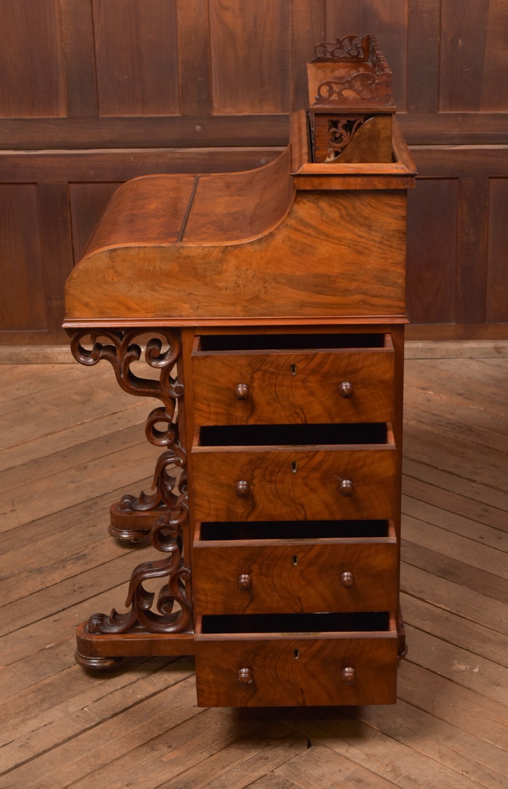 A Victorian burr walnut piano top Davenport desk featuring a carved fretwork gallery, sloped writing lid, scroll front supports, and side-opening drawers. View XIX