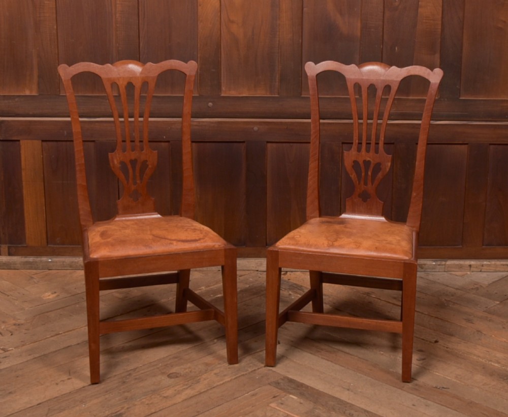 A matching pair of warm brown walnut side chairs with pierced vasiform splats, shaped crest rails, and upholstered drop-in seats supported by square legs with H-stretchers.