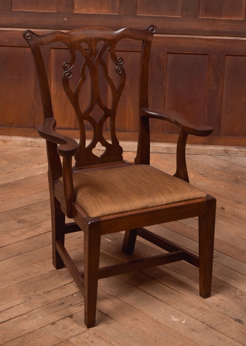 A dark hardwood open armchair featuring a pierced carved back splat, curved armrests, and a textured brown upholstered drop-in seat.
