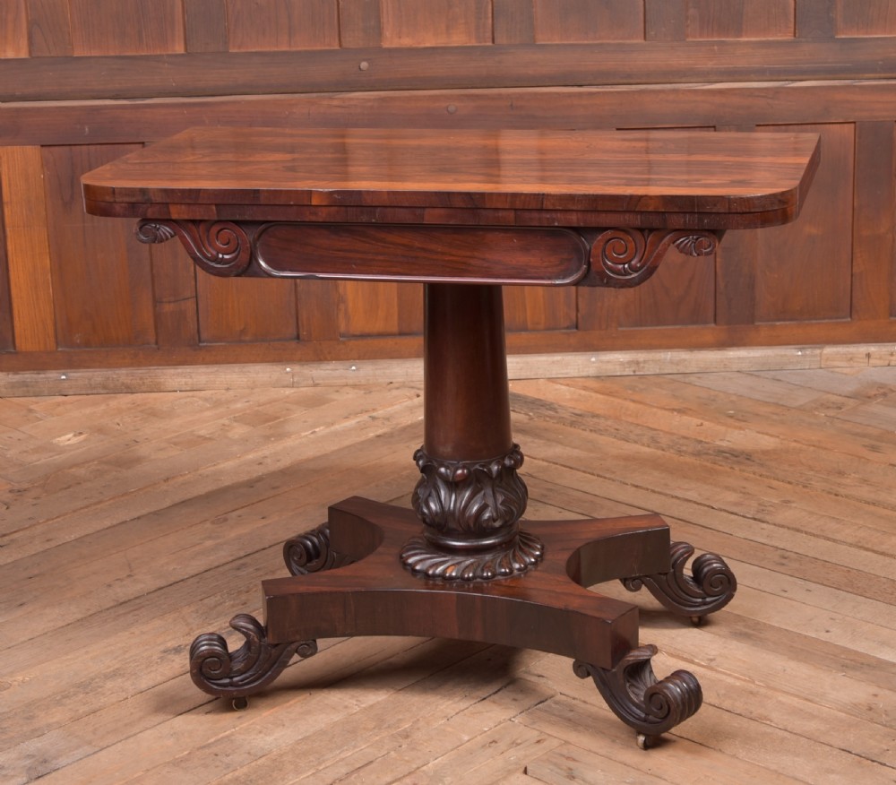 A Victorian rosewood fold-over card table featuring a rectangular swivel top, carved frieze, central column support, and a quadform base with scroll feet.