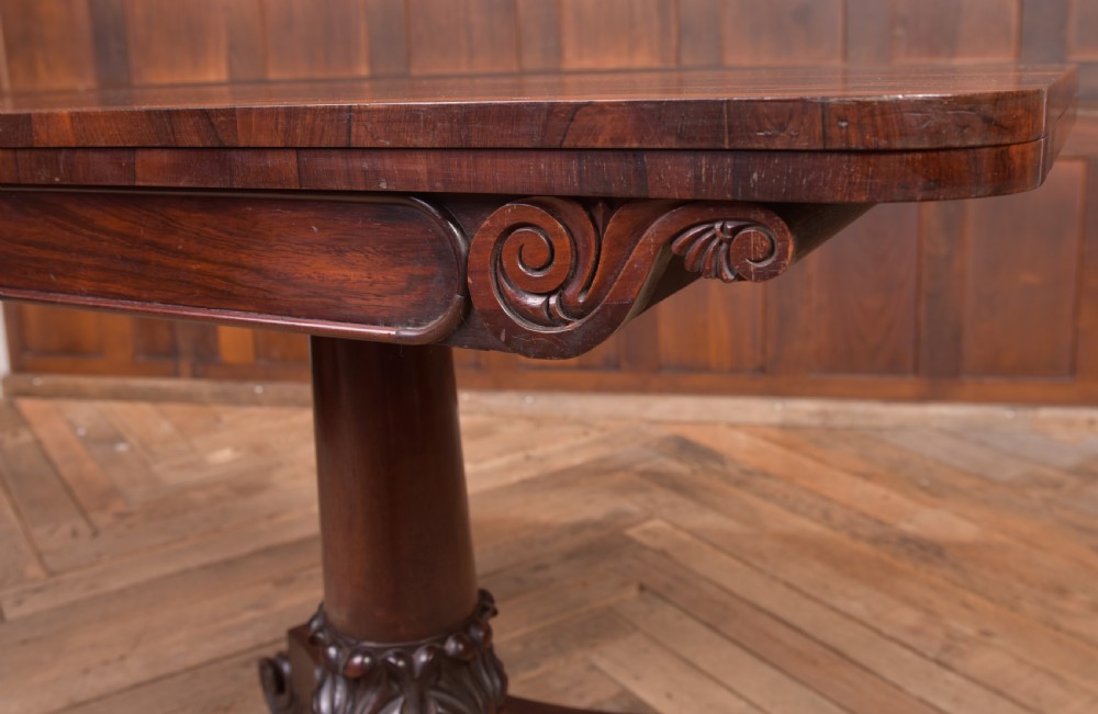 A Victorian rosewood fold-over card table featuring a rectangular swivel top, carved frieze, central column support, and a quadform base with scroll feet. View III