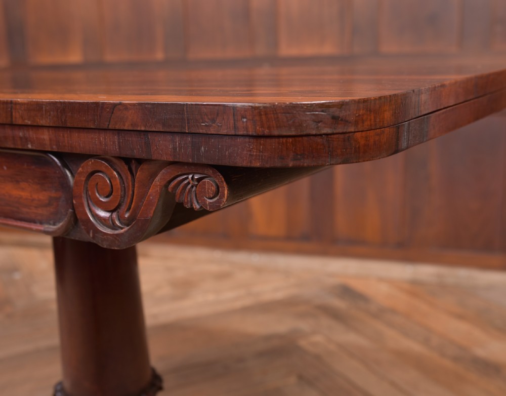 A Victorian rosewood fold-over card table featuring a rectangular swivel top, carved frieze, central column support, and a quadform base with scroll feet. View VI