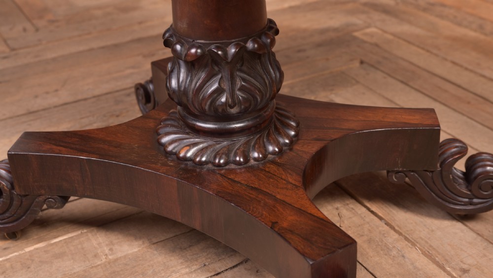 A Victorian rosewood fold-over card table featuring a rectangular swivel top, carved frieze, central column support, and a quadform base with scroll feet. View IX