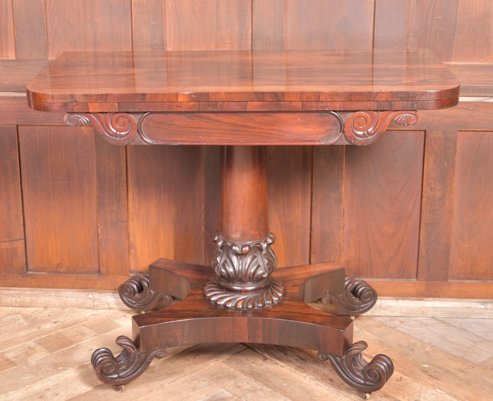 A Victorian rosewood fold-over card table featuring a rectangular swivel top, carved frieze, central column support, and a quadform base with scroll feet. View X