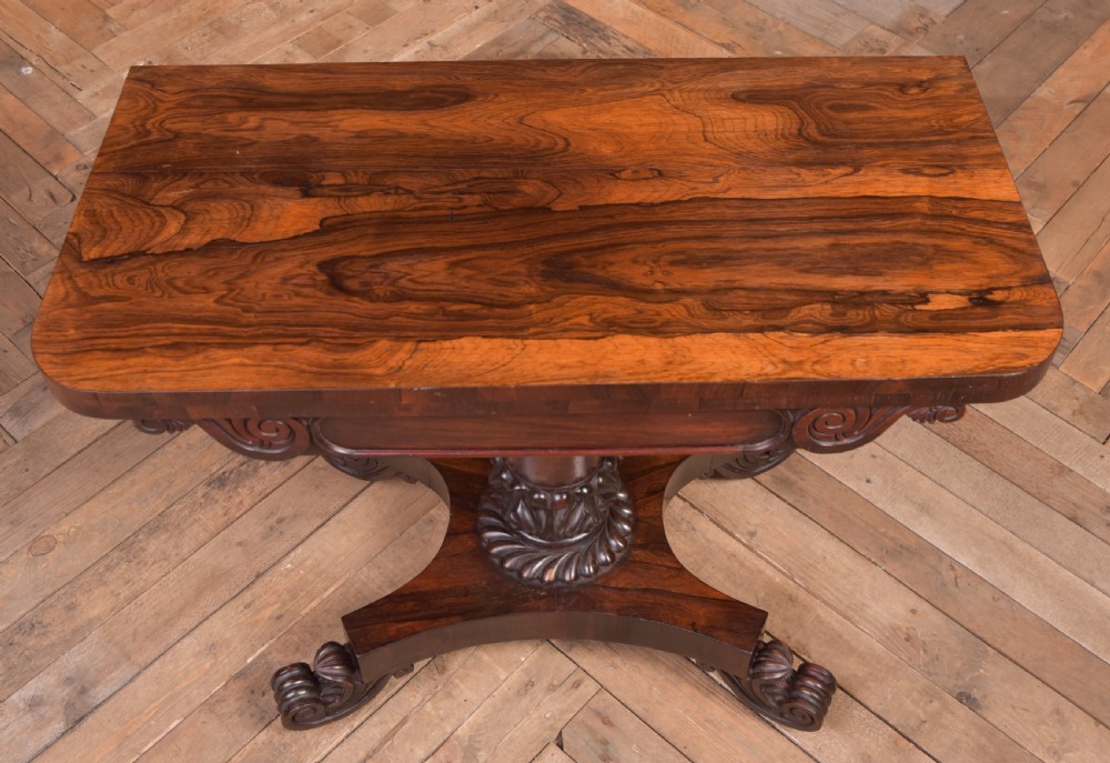 A Victorian rosewood fold-over card table featuring a rectangular swivel top, carved frieze, central column support, and a quadform base with scroll feet. View XIV
