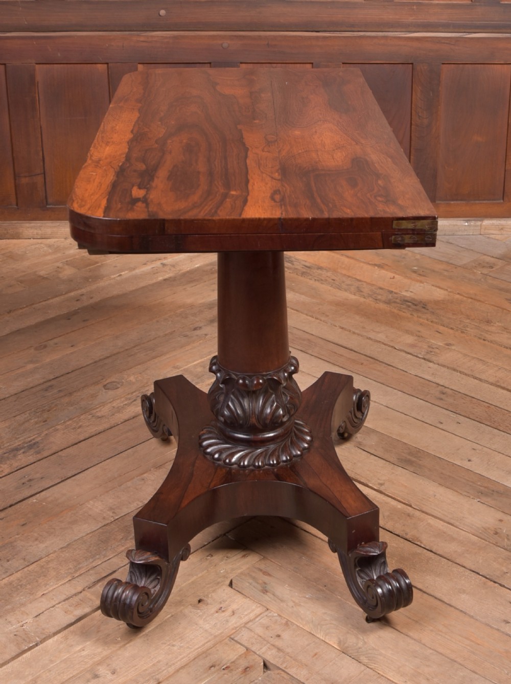 A Victorian rosewood fold-over card table featuring a rectangular swivel top, carved frieze, central column support, and a quadform base with scroll feet. View XV