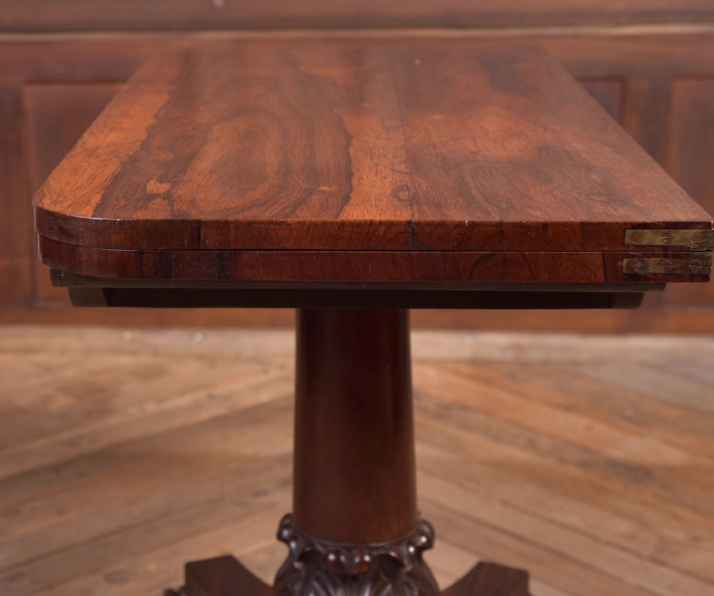 A Victorian rosewood fold-over card table featuring a rectangular swivel top, carved frieze, central column support, and a quadform base with scroll feet. View XVI