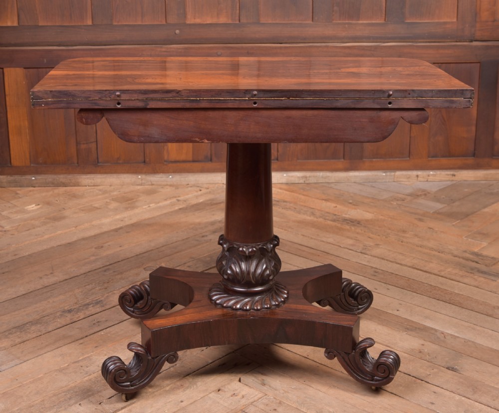A Victorian rosewood fold-over card table featuring a rectangular swivel top, carved frieze, central column support, and a quadform base with scroll feet. View XVII