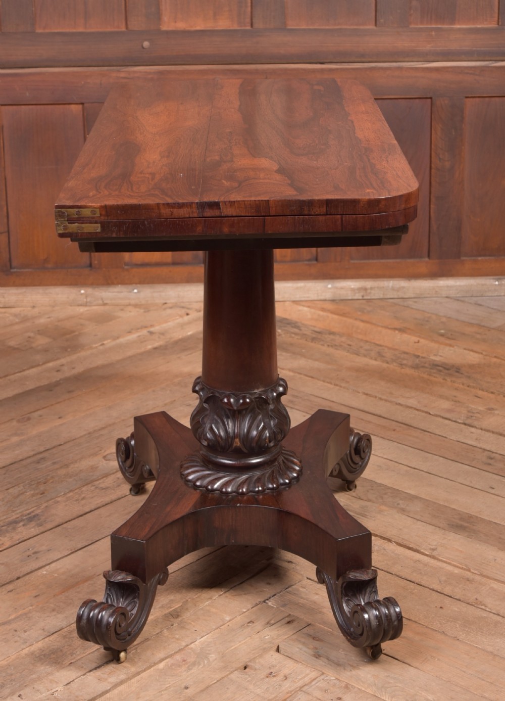 A Victorian rosewood fold-over card table featuring a rectangular swivel top, carved frieze, central column support, and a quadform base with scroll feet. View XVIII