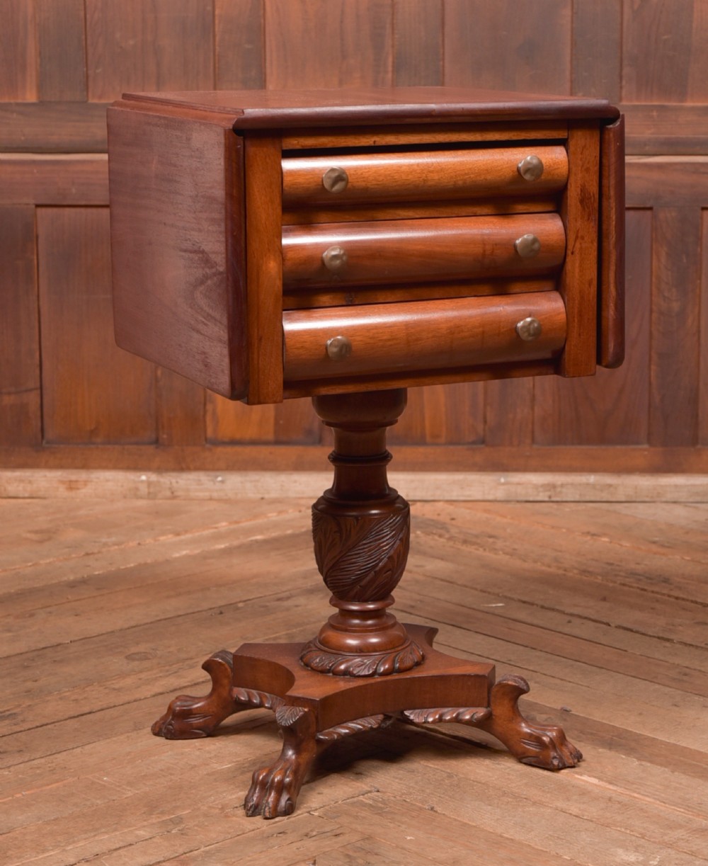 A Victorian mahogany drop-leaf worktable featuring three convex drawers, a carved pedestal column, and a quadruped base with claw feet.