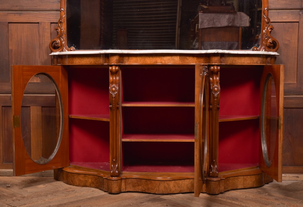 A Victorian burr walnut mirror-back credenza featuring a shaped white marble top, carved scrollwork crest, and three oval glazed cabinet doors revealing red fabric lining. View II