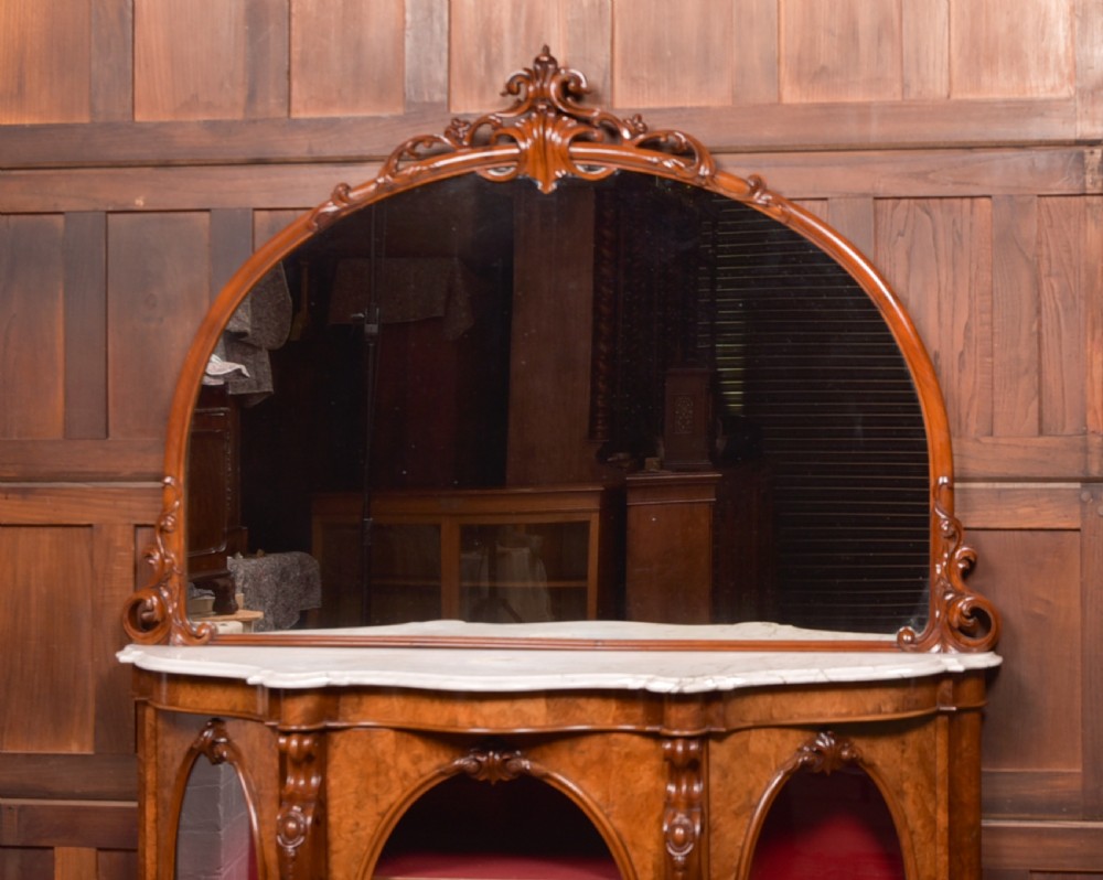A Victorian burr walnut mirror-back credenza featuring a shaped white marble top, carved scrollwork crest, and three oval glazed cabinet doors revealing red fabric lining. View V