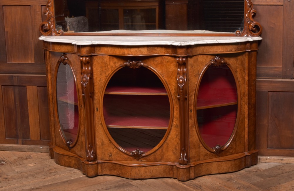 A Victorian burr walnut mirror-back credenza featuring a shaped white marble top, carved scrollwork crest, and three oval glazed cabinet doors revealing red fabric lining. View VII