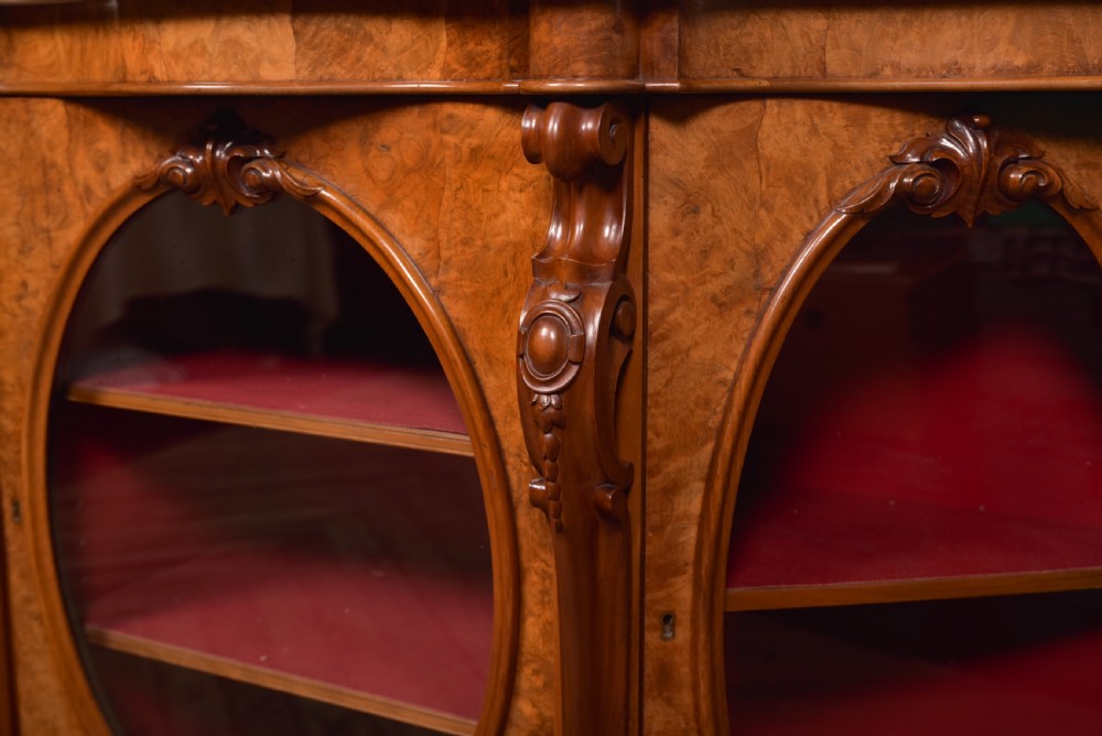 A Victorian burr walnut mirror-back credenza featuring a shaped white marble top, carved scrollwork crest, and three oval glazed cabinet doors revealing red fabric lining. View VIII