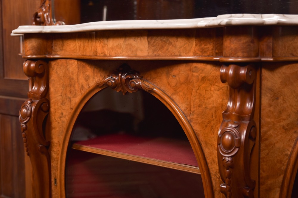 A Victorian burr walnut mirror-back credenza featuring a shaped white marble top, carved scrollwork crest, and three oval glazed cabinet doors revealing red fabric lining. View IX