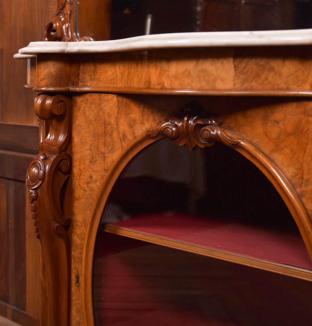 A Victorian burr walnut mirror-back credenza featuring a shaped white marble top, carved scrollwork crest, and three oval glazed cabinet doors revealing red fabric lining. View X