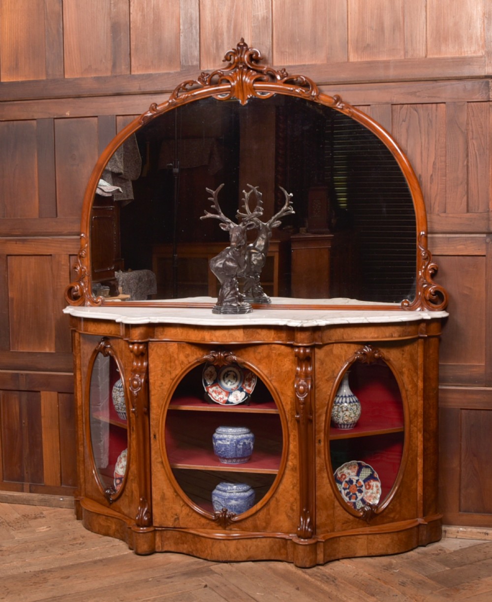 A Victorian burr walnut mirror-back credenza featuring a shaped white marble top, carved scrollwork crest, and three oval glazed cabinet doors revealing red fabric lining. View XIV