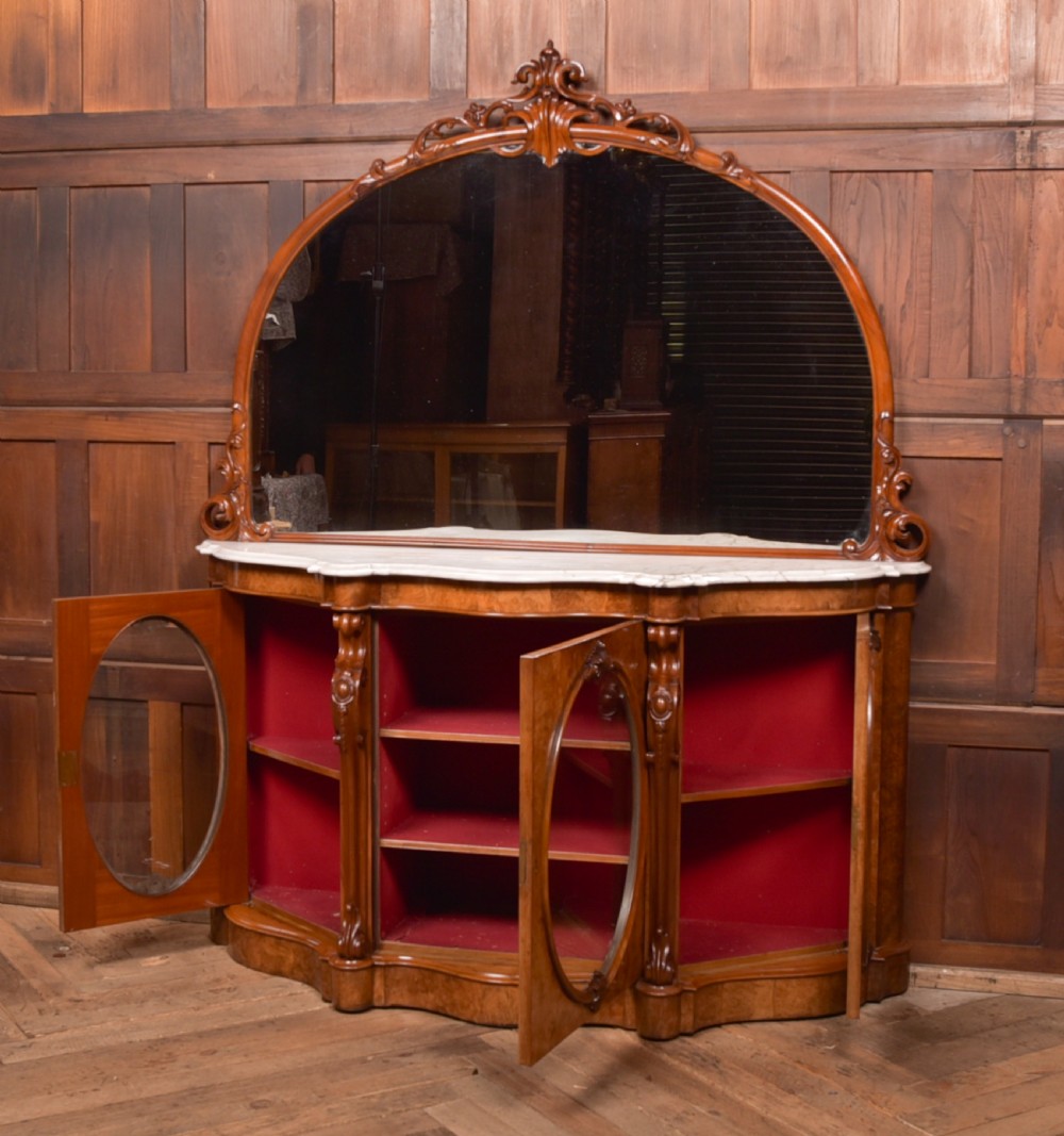 A Victorian burr walnut mirror-back credenza featuring a shaped white marble top, carved scrollwork crest, and three oval glazed cabinet doors revealing red fabric lining. View XVI