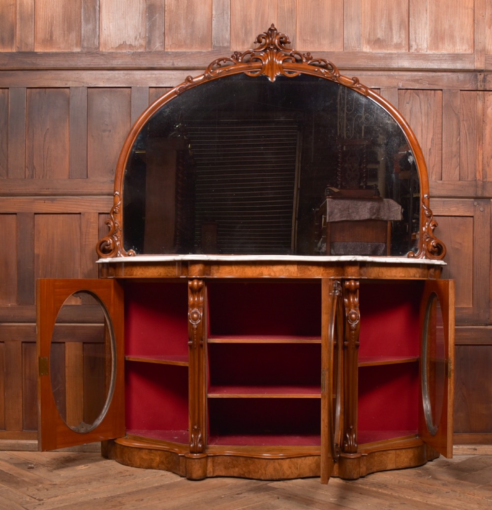 A Victorian burr walnut mirror-back credenza featuring a shaped white marble top, carved scrollwork crest, and three oval glazed cabinet doors revealing red fabric lining. View XVII
