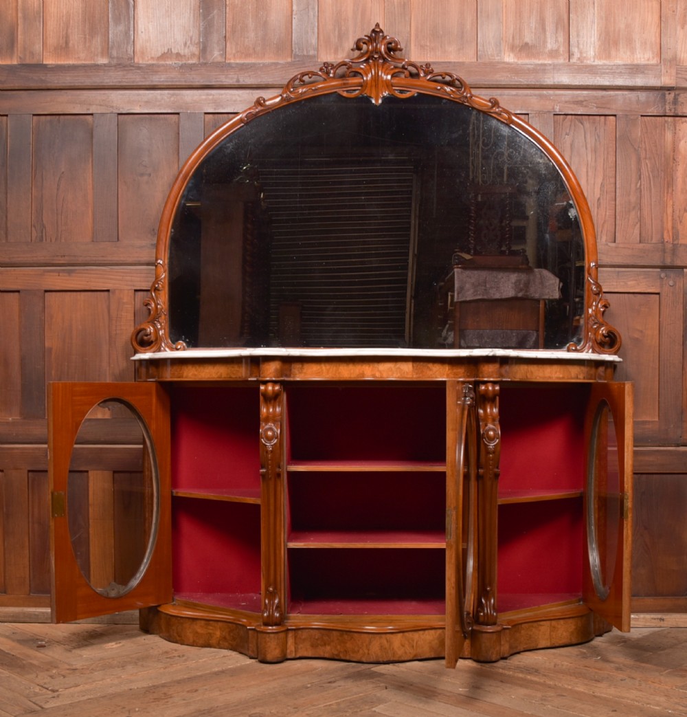 A Victorian burr walnut mirror-back credenza featuring a shaped white marble top, carved scrollwork crest, and three oval glazed cabinet doors revealing red fabric lining. View XVIII