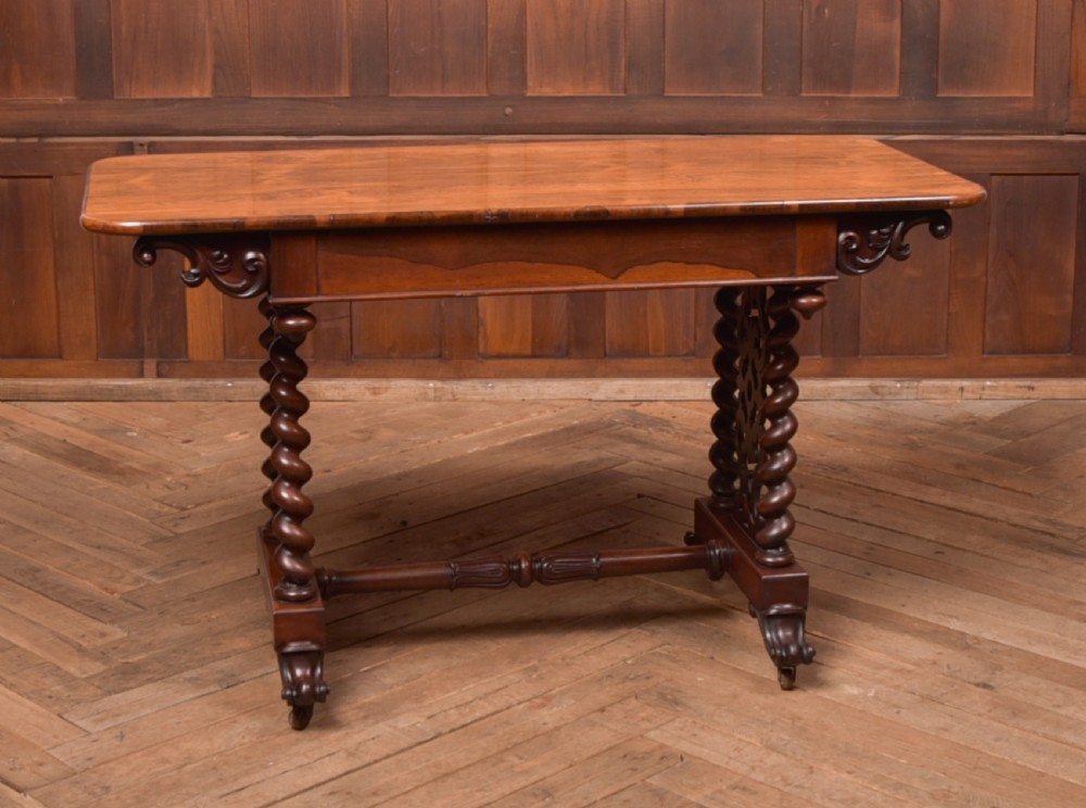 A Victorian wooden side table featuring a rectangular top with rounded corners, carved scroll brackets, double barley twist legs, a central stretcher, and castors.