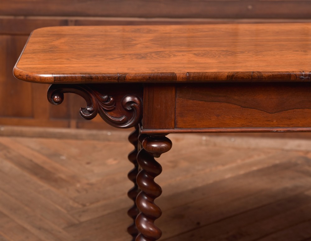 A Victorian wooden side table featuring a rectangular top with rounded corners, carved scroll brackets, double barley twist legs, a central stretcher, and castors. View III