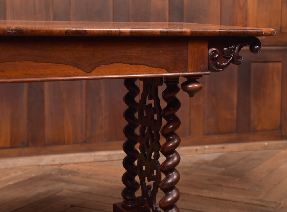 A Victorian wooden side table featuring a rectangular top with rounded corners, carved scroll brackets, double barley twist legs, a central stretcher, and castors. View VI