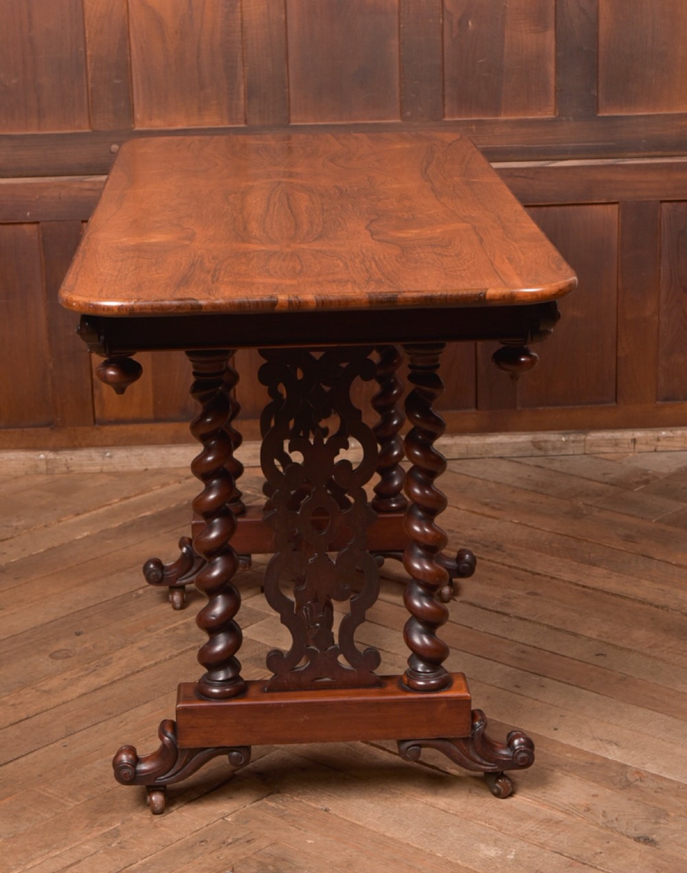 A Victorian wooden side table featuring a rectangular top with rounded corners, carved scroll brackets, double barley twist legs, a central stretcher, and castors. View IX