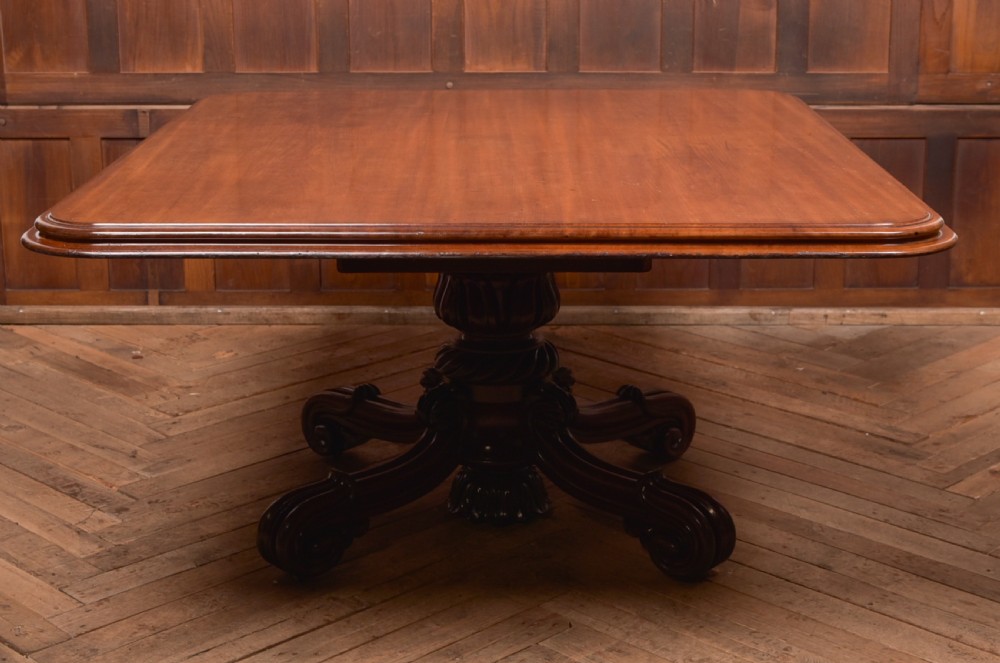 A Victorian mahogany tilt-top table featuring a polished rectangular top with rounded corners set upon a carved pedestal stem with quadruped scrolled legs.